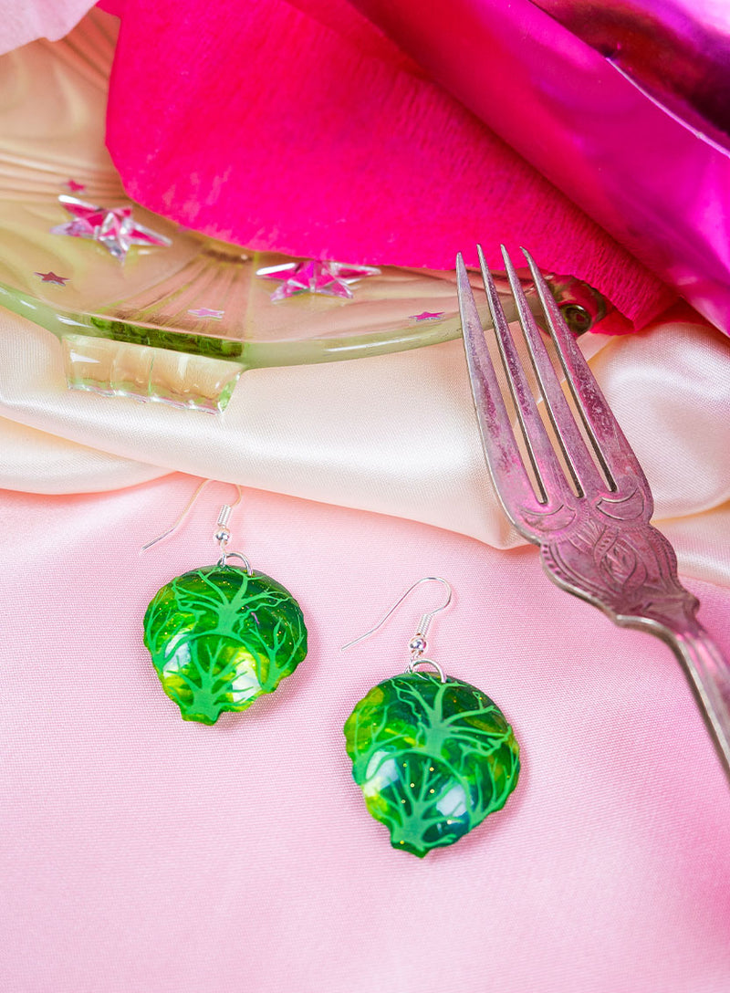 Brussels Sprout Earrings made from glitter-flecked green acrylic placed on a table setting