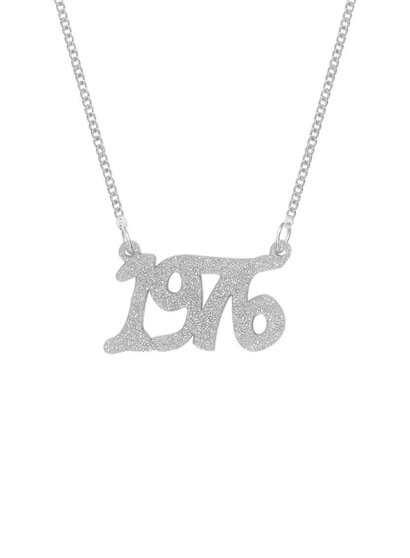 A silver chain personalised Name Necklace featuring a glittery, stylised '1976' pendant in silver dust acrylic, shown against a plain white background.