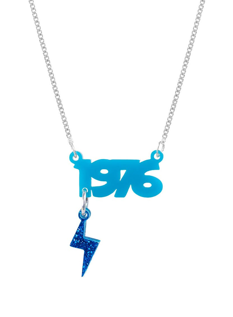 A custom Name Necklace on a silver metal chain, featuring a bright blue '1976' text pendant and a dangling glittery blue lightning bolt charm, shown against a plain white background.