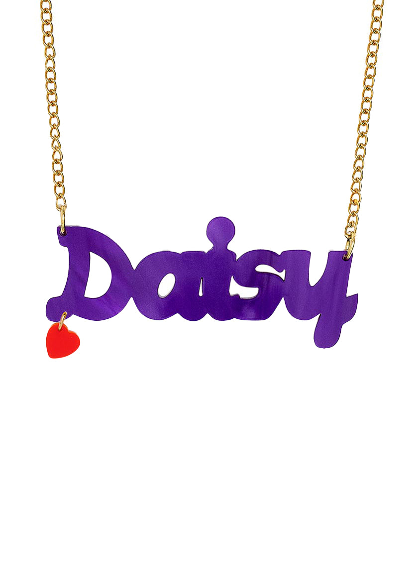 A Name necklace in limited edition plum pearl spelling 'Daisy' on a gold chain, with a small red heart charm hanging from the left side, shown against a plain white background.