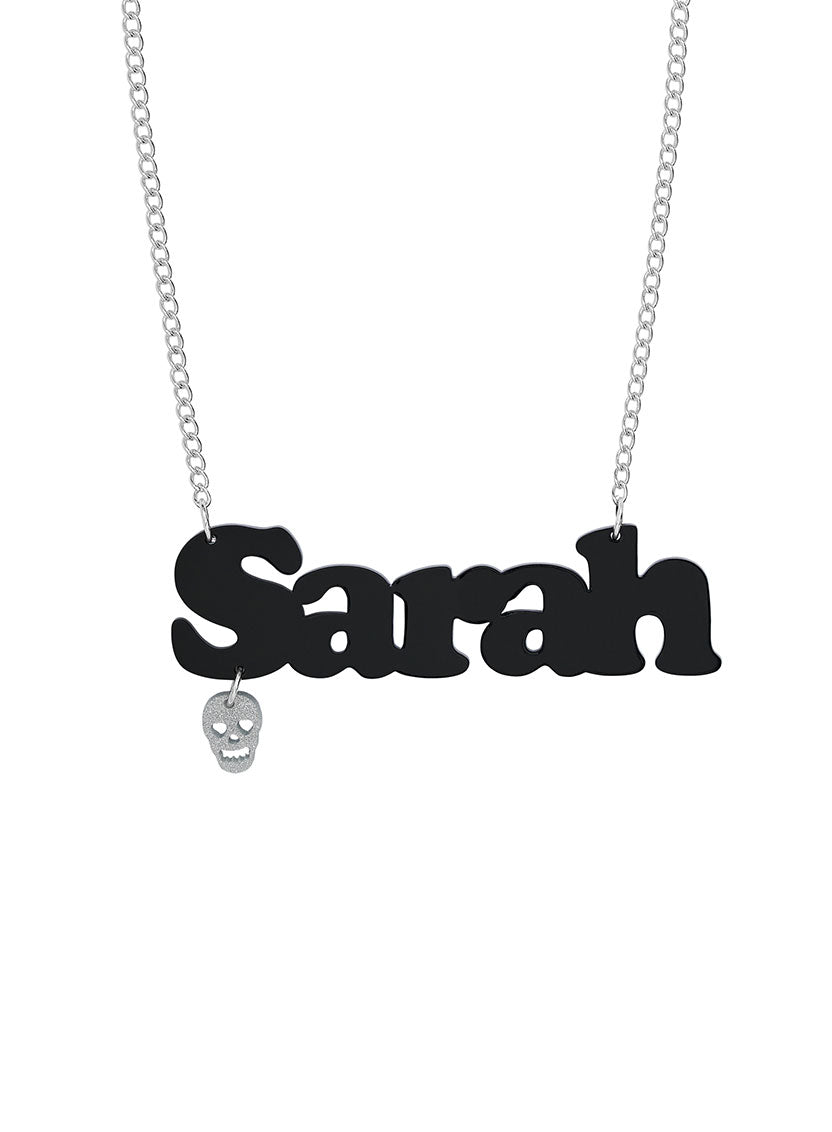 A custom name necklace with a black nameplate pendant spelling 'Sarah' and a small dangling silver skull charm, with a silver chain, shown on a plain white background.