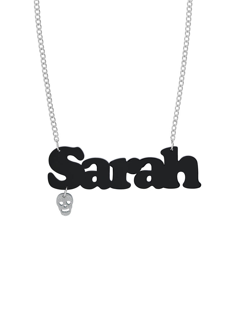 A custom name necklace with a black nameplate pendant spelling 'Sarah' and a small dangling silver skull charm, with a silver chain, shown on a plain white background.