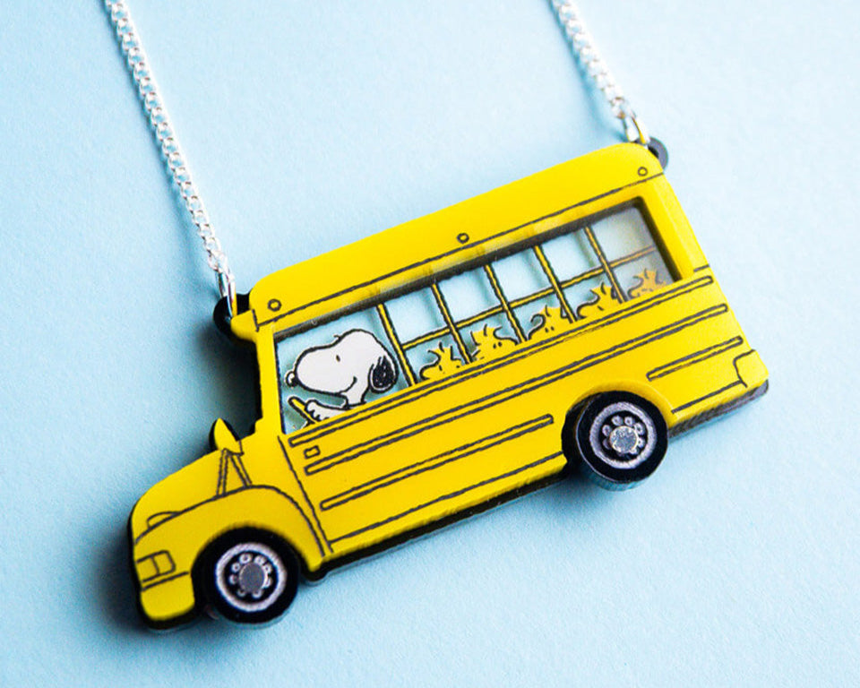 Yellow school bus pendant with Snoopy driving and Woodstocks on board, on a chain against a light blue background.