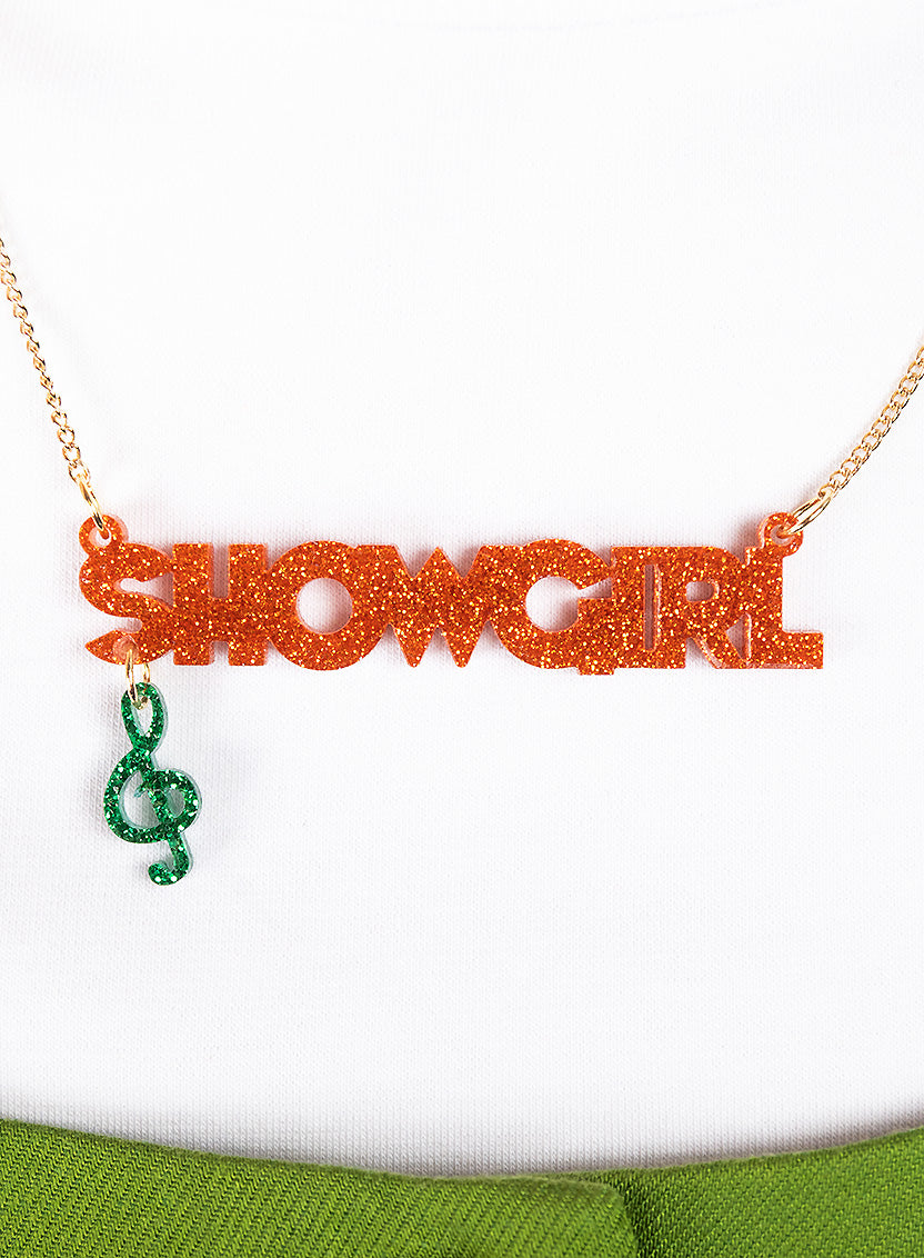 Tatty Devine Name Necklace with 'SHOWGIRL' in orange glitter and green pendant on a white background.